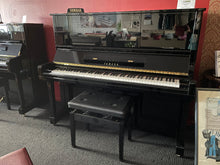Load image into Gallery viewer, Yamaha upright piano in a showroom setting with a bench