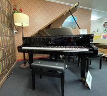 Load image into Gallery viewer, Black grand piano in a room with patterned wallpaper and a lamp.
