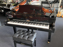 Load image into Gallery viewer, Black piano with a matching black bench in a showroom setting
