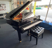 Load image into Gallery viewer, Black grand piano with a bench in a showroom setting
