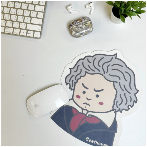 Mousepad with a cartoon Beethoven with gray hair on a desk with a keyboard and aplant.