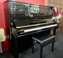 Load image into Gallery viewer, Black upright piano with a bench in a room with red walls and decorative elements.
